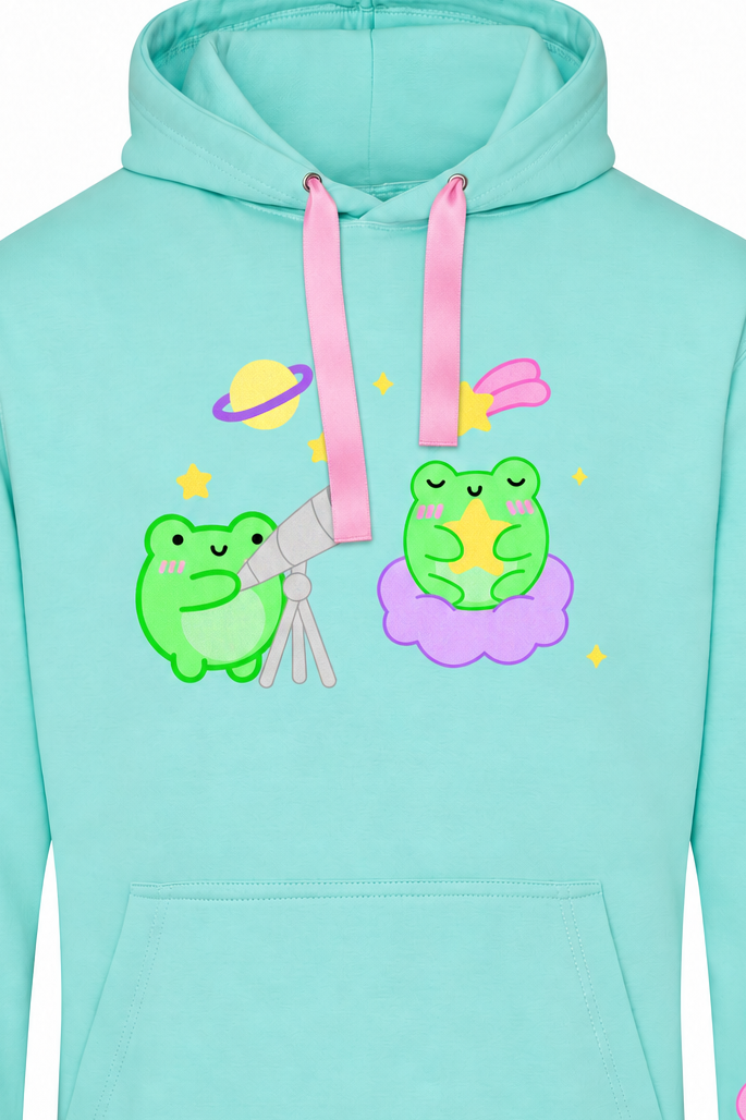 A mint green pullover hoodie featuring a cute cartoon graphic of two green frogs with pink and yellow space-themed accessories, with matching graphics printed on both sleeves.