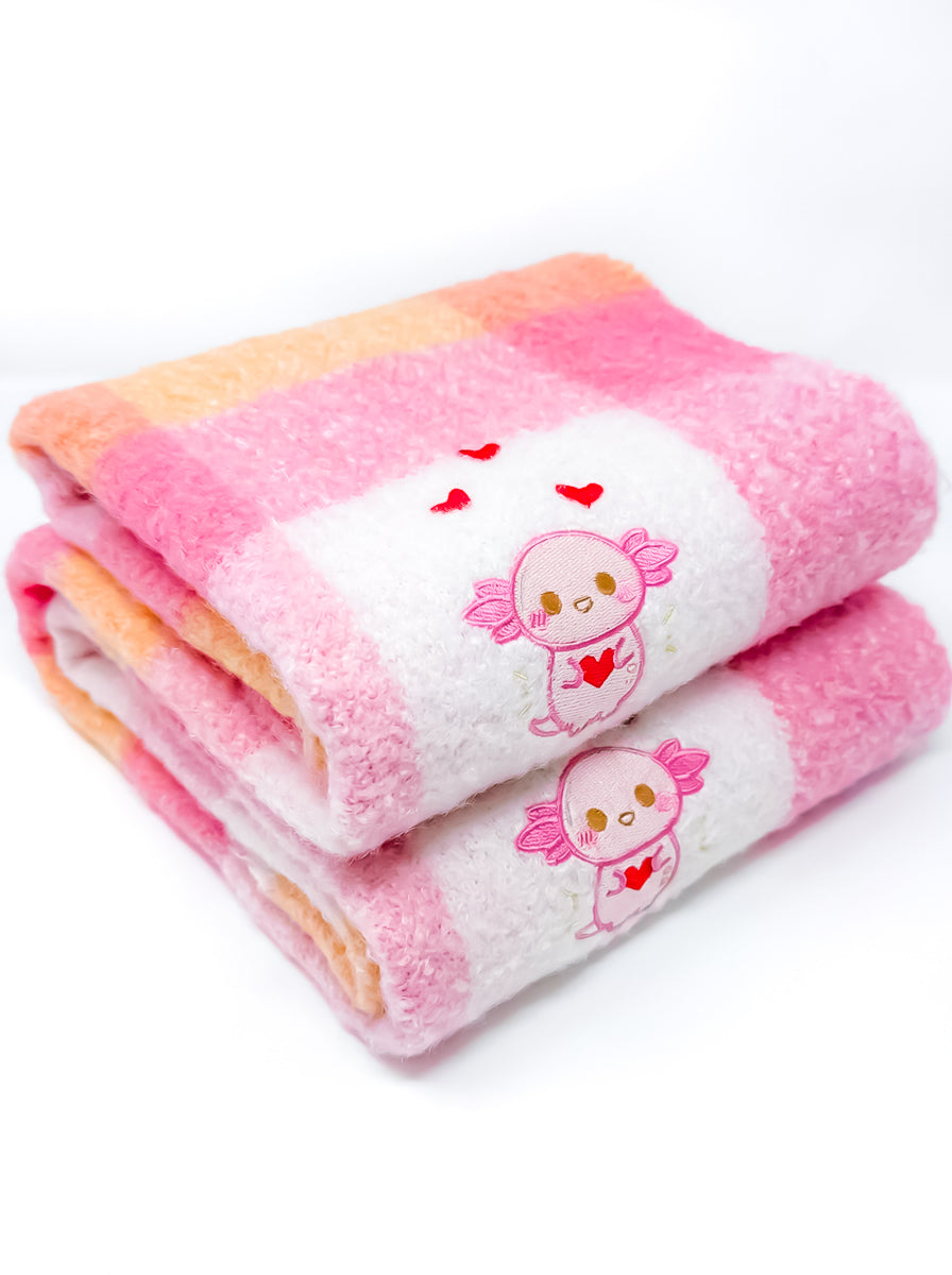 Folded pink and orange scarf with cartoon character xoxi the axolotl and heart design on a white background