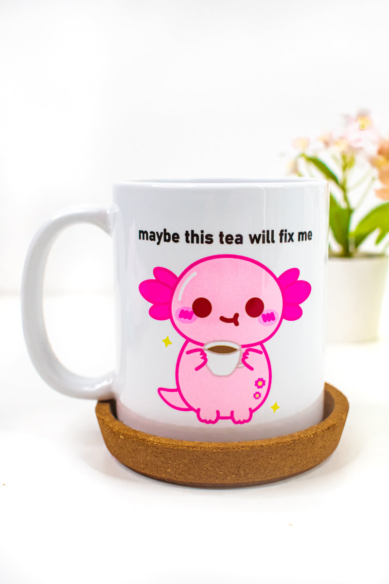 A white ceramic mug with a design of xoxi the axolotl holding a cup and the text 'maybe this tea will fix me'.