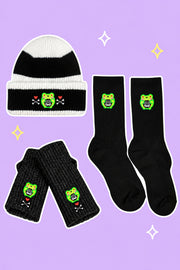 Skelly Albert Winter Survival Bundle: one black-and-white striped Skelly Albert beanie, one pair black Skelly handwarmers, one pair black Skelly socks, on a simple pastel background with white outlines and small sparkles.