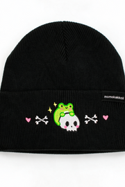 A black ribbed knit beanie hat featuring a cute embroidered design on the front cuff. The design shows a green frog sitting on a white skull, flanked by pink hearts and white crossed bones.