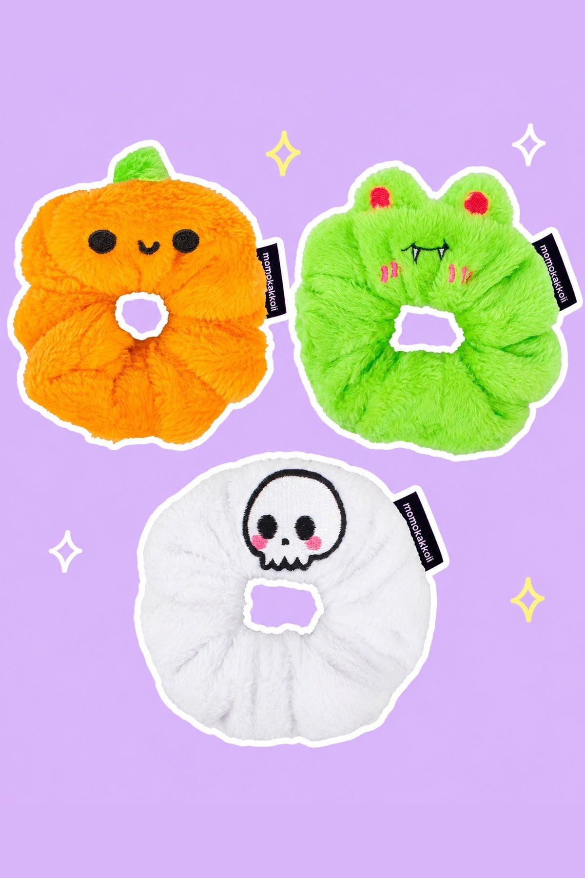 Spooky Scrunchie Trio – Halloween Bundle: one orange Patch the Pumpkin scrunchie with cute round black eyes and curved smile (NOT jack-o-lantern), one lime green Vampire Albert scrunchie with red eyes and fangs, one white Cute Skull scrunchie, on a simple pastel background with white outlines and small sparkles.