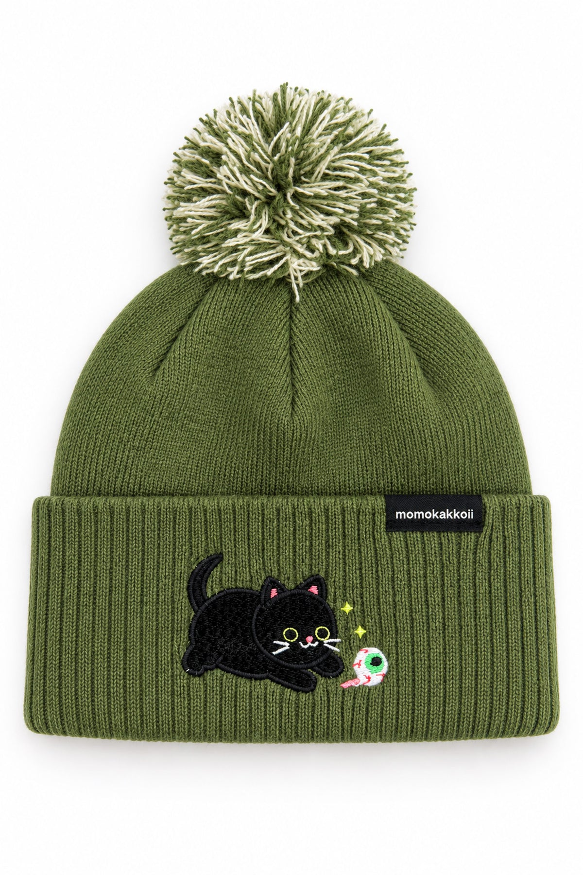An olive green knit beanie with a pom-pom on top and a folded cuff featuring an embroidered black cat and a small colorful moon, with a small black brand tag reading 'momakakoi' on the side.