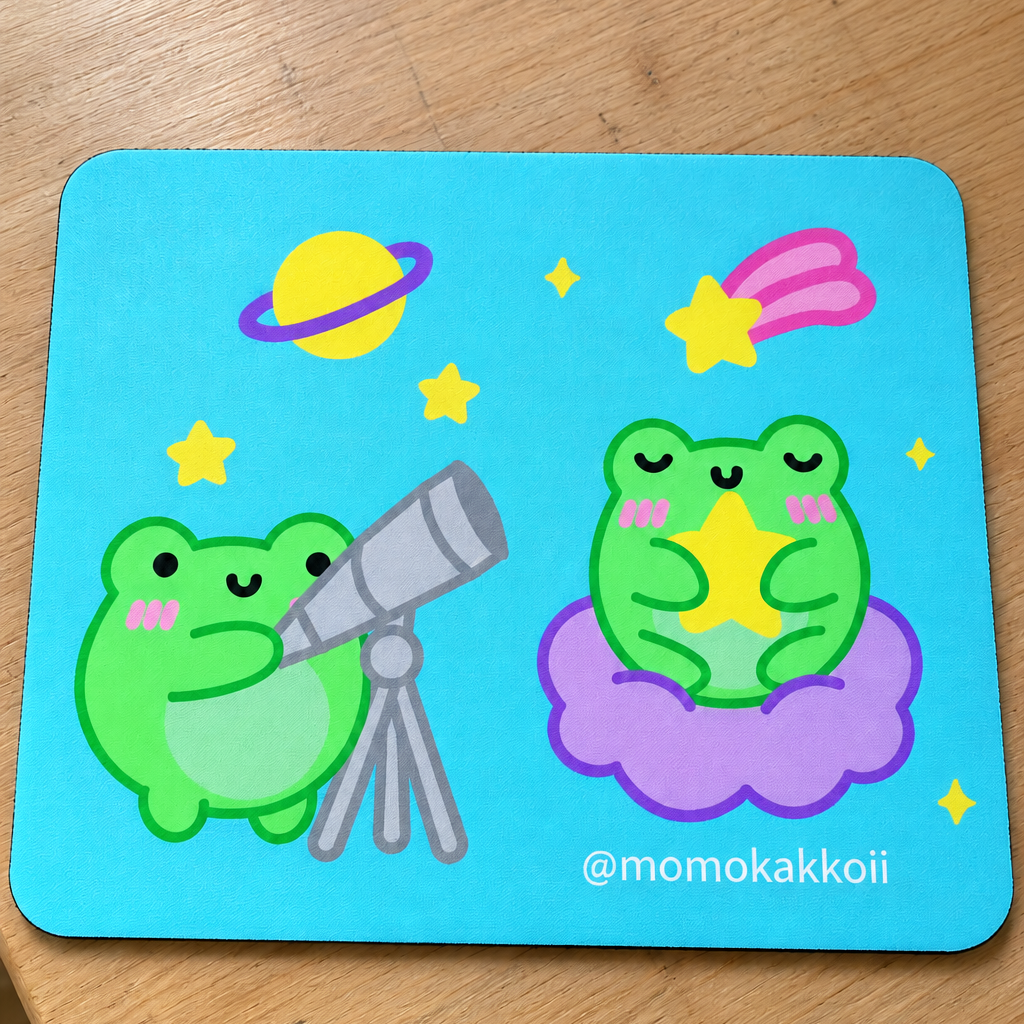 A square mouse pad with rounded corners featuring a cute cartoon design of two green frogs in a space theme, placed on a wooden table. The left frog holds a silver telescope, while the right frog sits on a purple cloud with a yellow star.